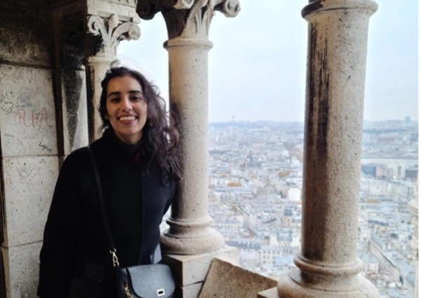 Maha Malik poses next to pillars overlooking a city. 