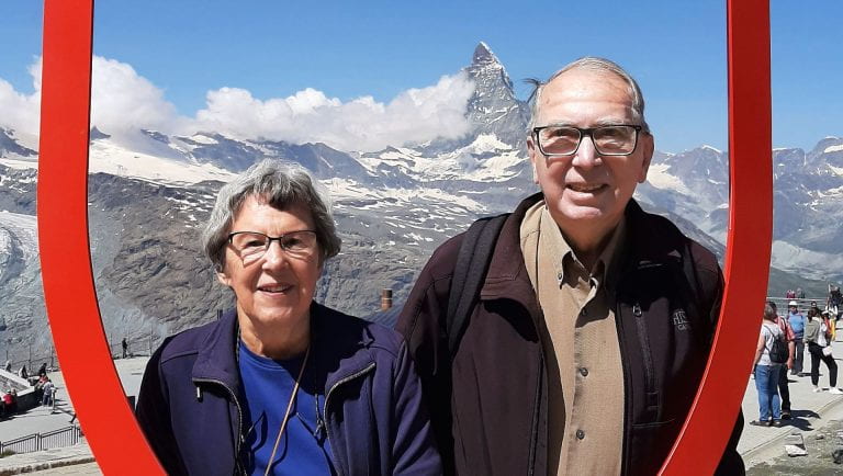 David Shinn at Grand Tour of Switzerland - there are snowcapped mountains behind him and he is standing with a woman