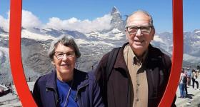 David Shinn at Grand Tour of Switzerland - there are snowcapped mountains behind him and he is standing with a woman